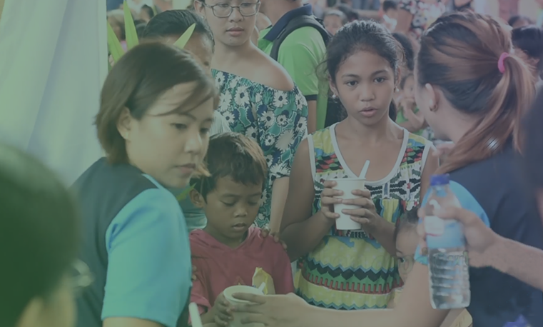 A woman giving soup in a cup to the children